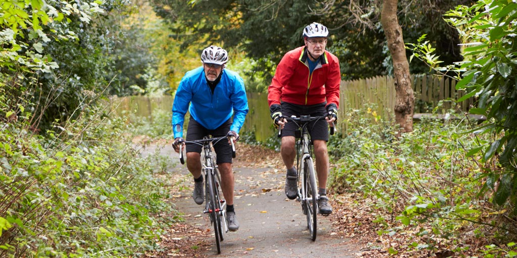 Two men riding bikes along a woodland path.