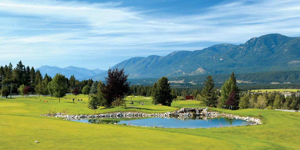 Radium Golf Course on a bright sunny day with green grass, a blue pond and mountains in the background.