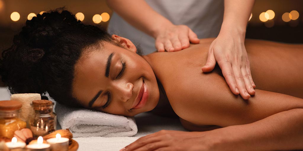A smiling woman lying on her front receiving a massage by a pair of hands belonging to an unseen person.
